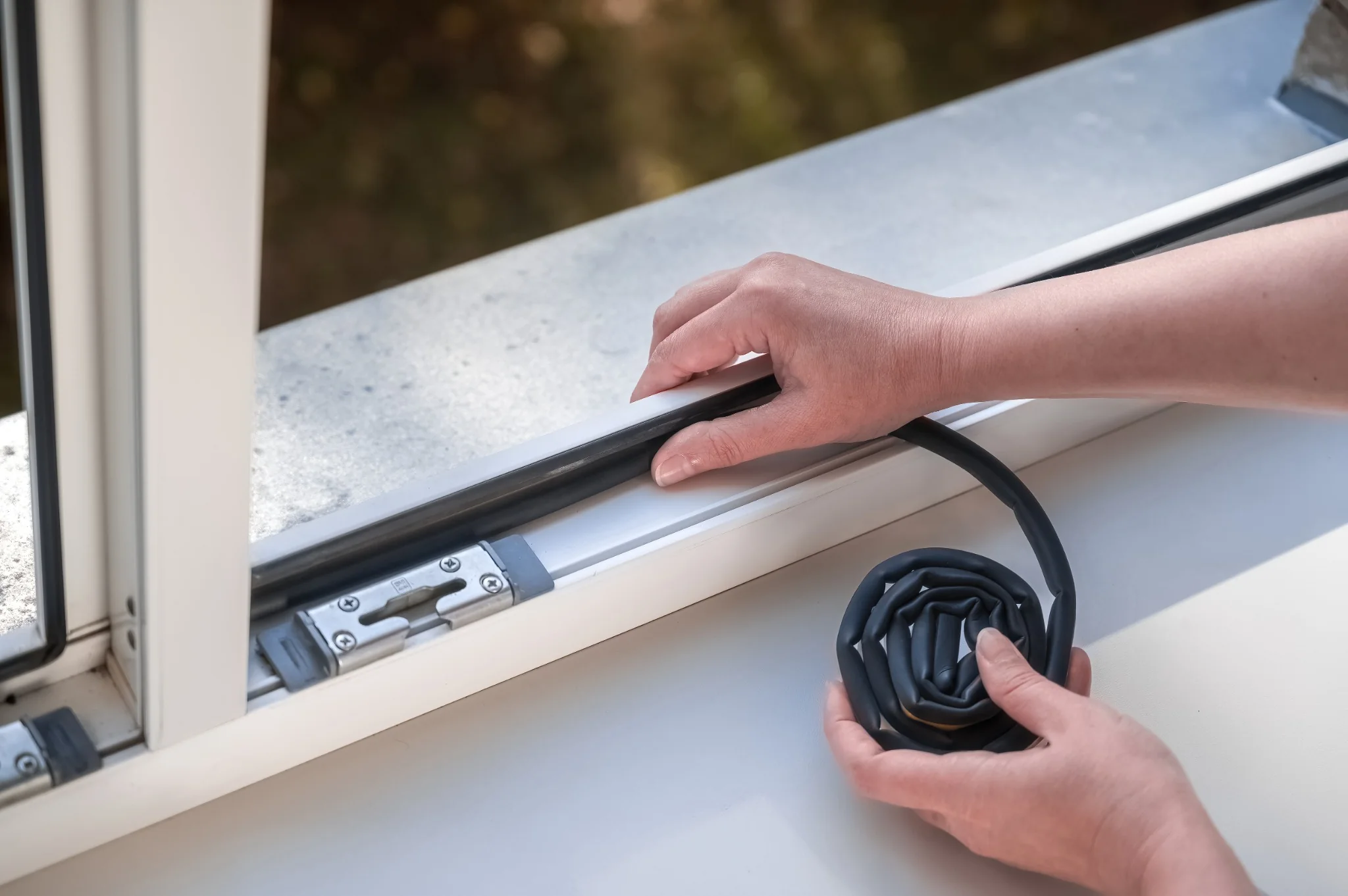 Hands fitting black weatherstripping into a residential window frame