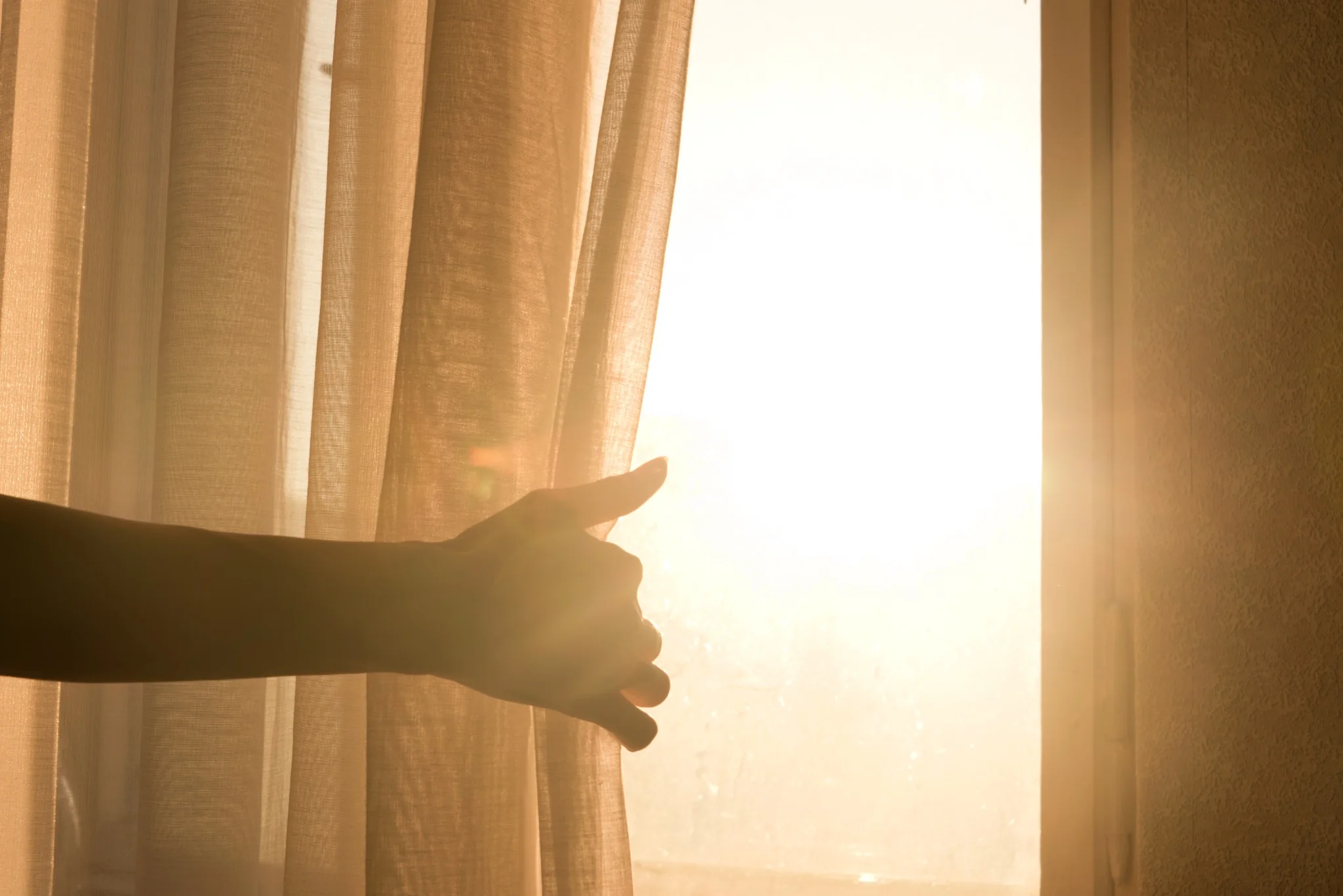 Warm sunlight shining through curtains beside a residential window
