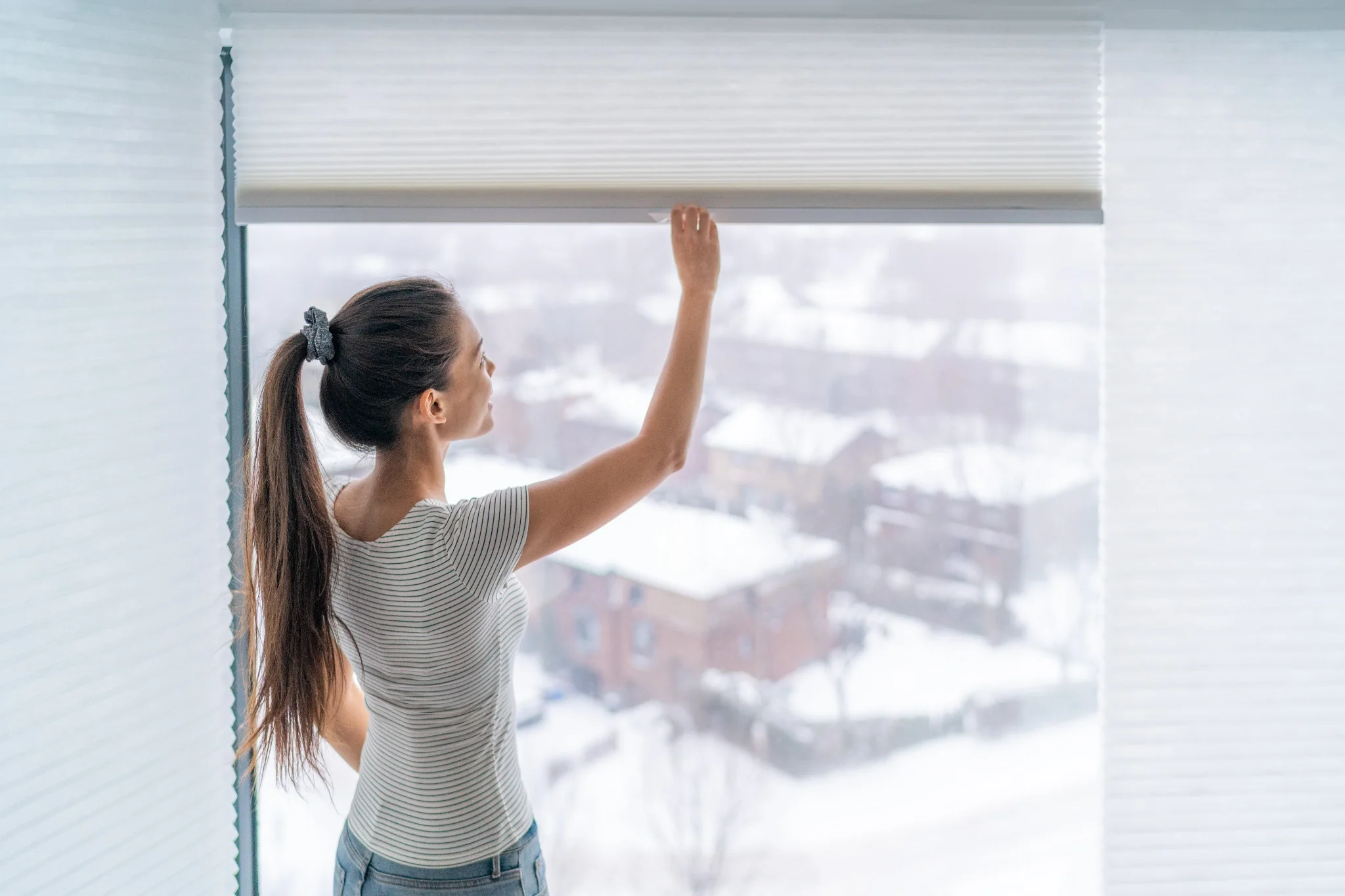 Homeowner adjusting a window shade with snow visible outside